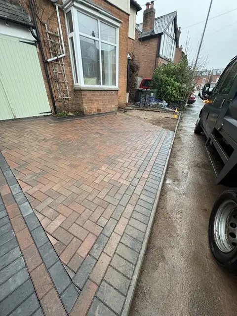 A block paved driveway with a contrasting border beside a parked car