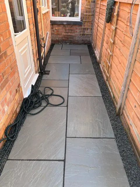 A narrow side passage paved in grey slabs with a gravel drainage strip